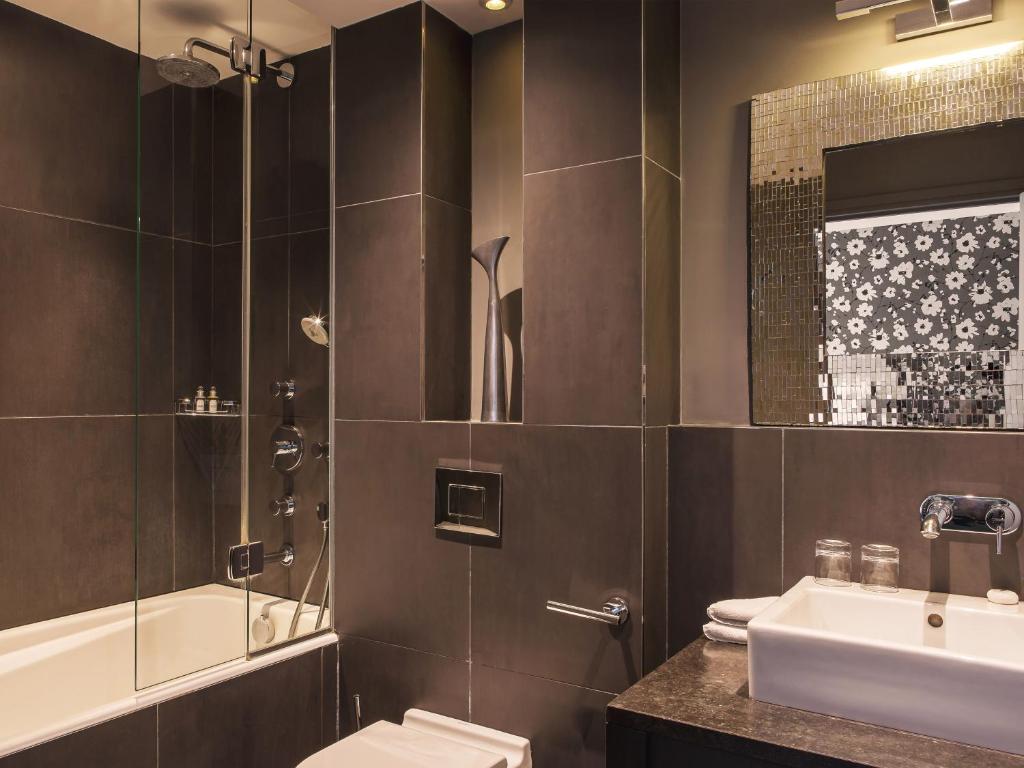 a bathroom with a toilet, sink, mirror and bath tub at New Hotel Roblin in Paris