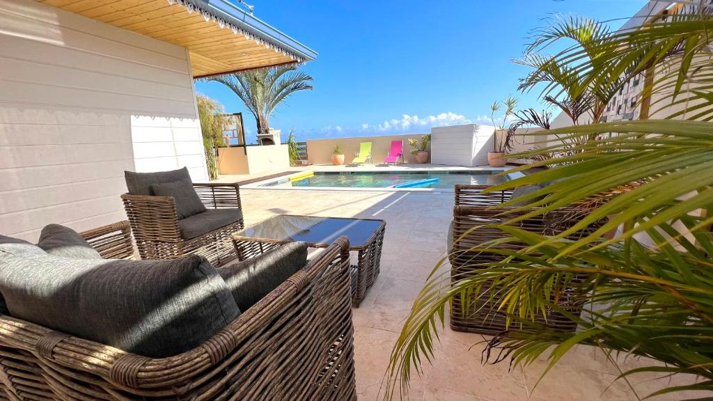 une terrasse avec des chaises en osier, une table et une piscine dans l'établissement Villa Horizon, à Saint-Joseph