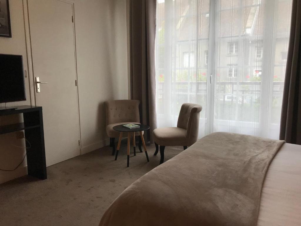 a bedroom with a bed and a chair and a television at Logis Hôtel-Restaurant Les Airelles in Neufchâtel-en-Bray