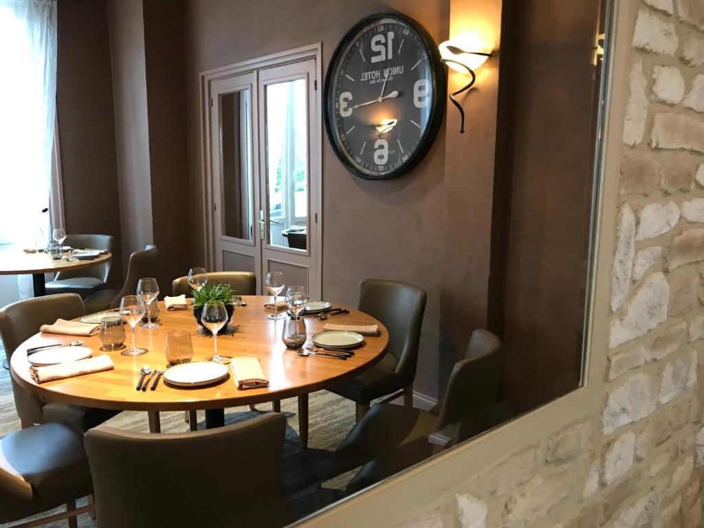 a table in a restaurant with a clock on the wall at Logis Hôtel-Restaurant Les Airelles in Neufchâtel-en-Bray
