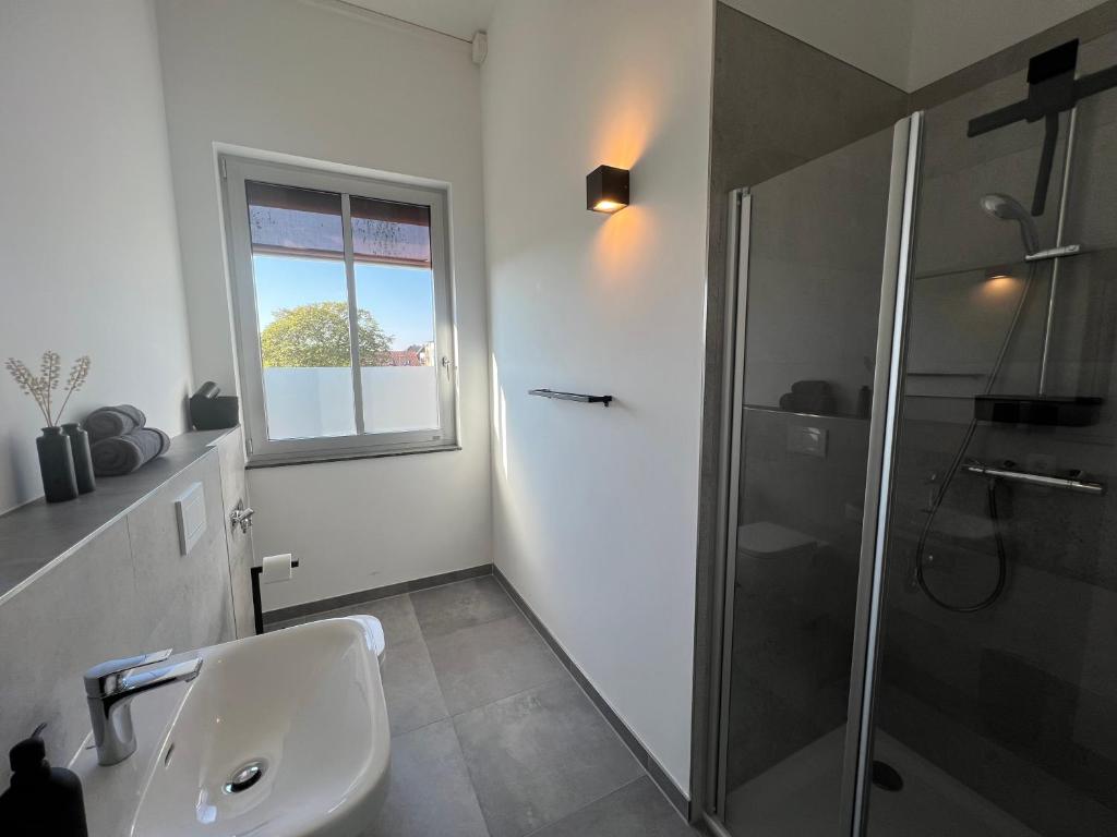 ein weißes Bad mit einer Dusche und einem Waschbecken in der Unterkunft Apartmenthaus Sassnitz Zum Stadthafen Apartment 10 in Sassnitz