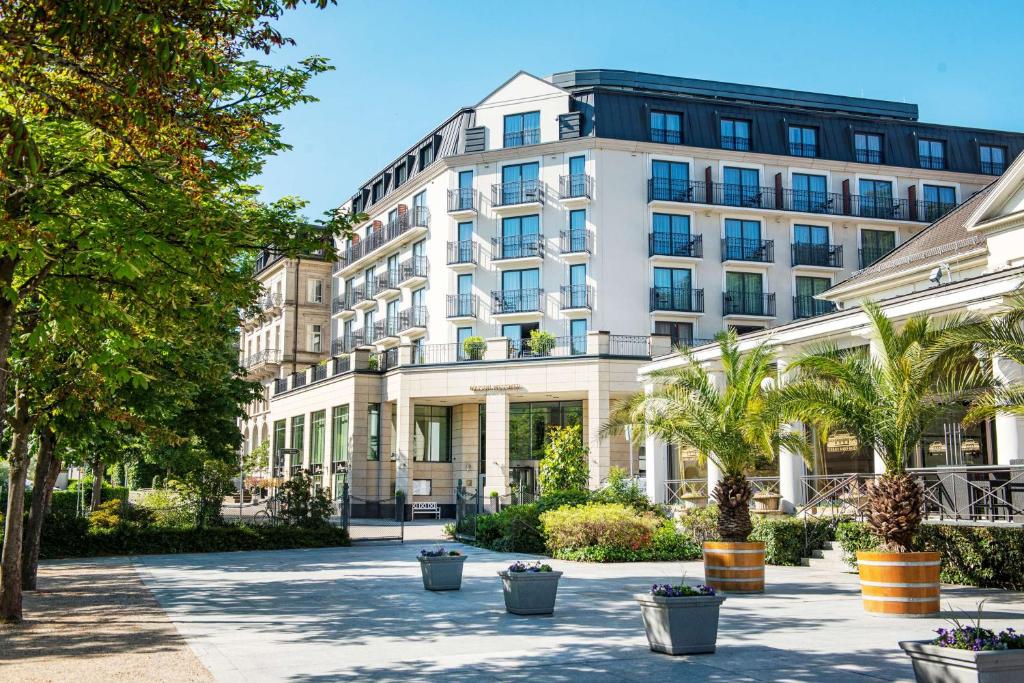 un grand bâtiment blanc avec des arbres devant lui dans l'établissement Maison Messmer - ein Mitglied der Hommage Luxury Hotels Collection, à Baden-Baden