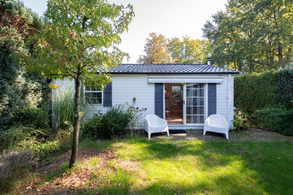 a tiny house with two white chairs in the yard at 84, gelegen in het rustige & bosrijke Oisterwijk! Met privétuin in Oisterwijk