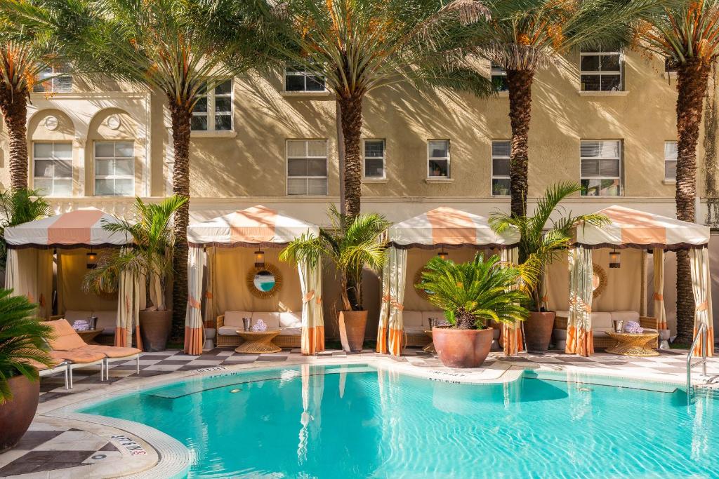 a swimming pool in front of a building with palm trees at The Plymouth South Beach in Miami Beach