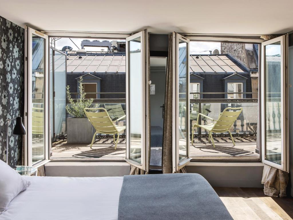 a bedroom with a bed and a balcony with chairs at New Hotel Roblin in Paris