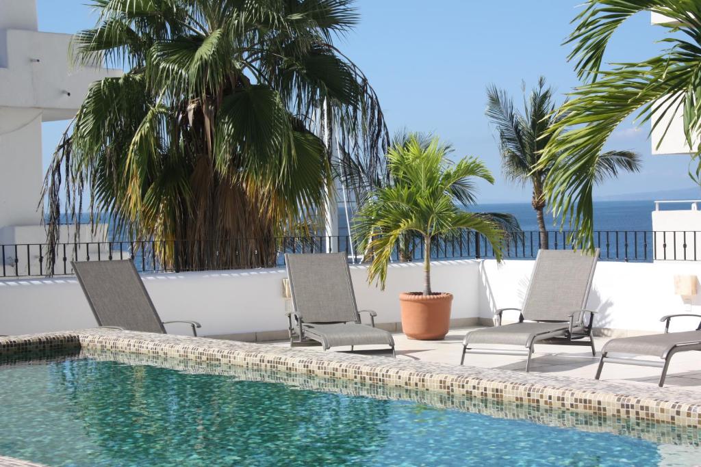 a swimming pool with two chairs and palm trees at Amapas Apartments Puerto Vallarta in Puerto Vallarta