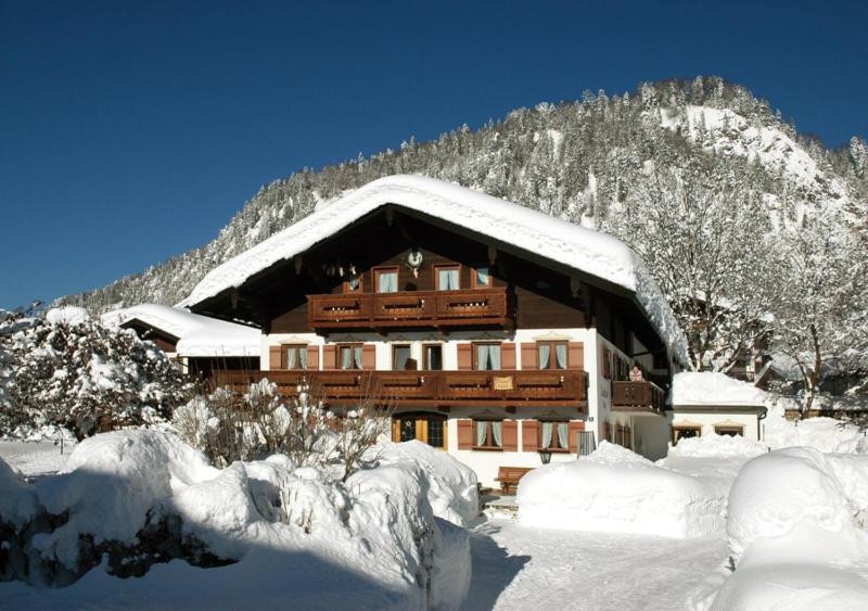 ein schneebedecktes Gebäude mit einem Berg im Hintergrund in der Unterkunft Landhaus Lengg in Reit im Winkl