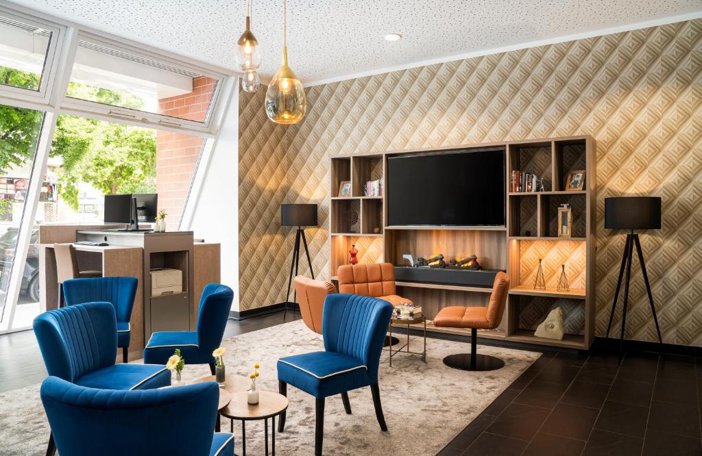 ein Wohnzimmer mit einem TV und blauen Stühlen in der Unterkunft Leonardo Hotel Berlin in Berlin