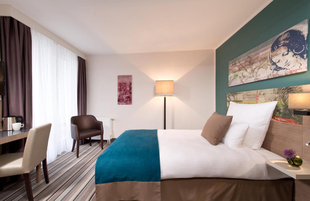 ミュンヘンにあるレオナルド ホテル ミュンヘン シティ オリンピアのベッドとデスクが備わるホテルルームです。