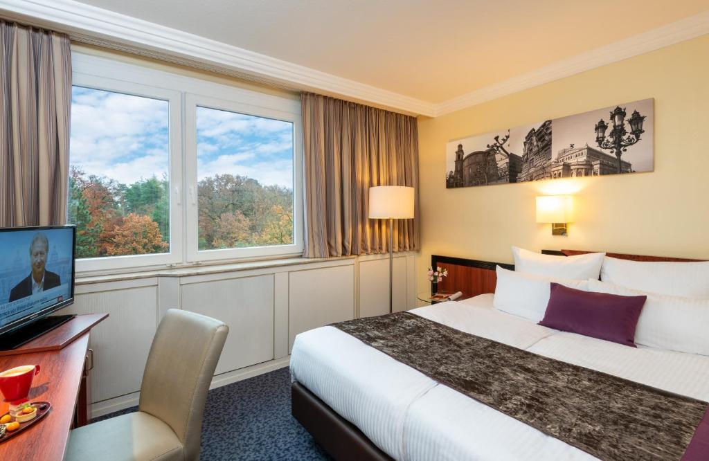 a hotel room with a bed and a desk and a tv at Leonardo Hotel Frankfurt City South in Frankfurt