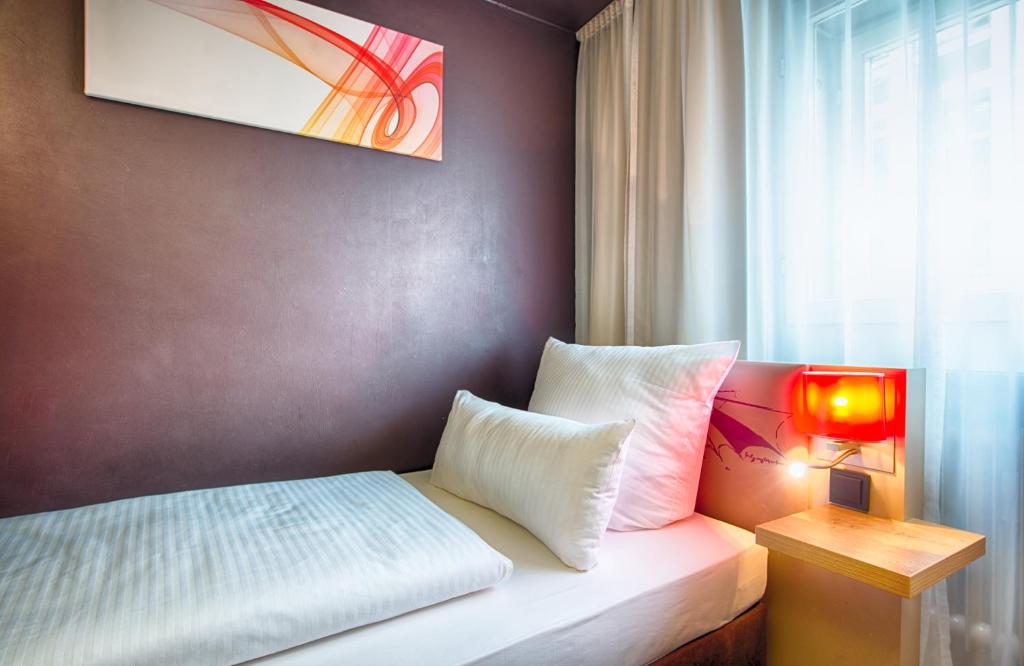 a bed with two pillows and a lamp next to a window at Leonardo Boutique Hotel Munich in Munich