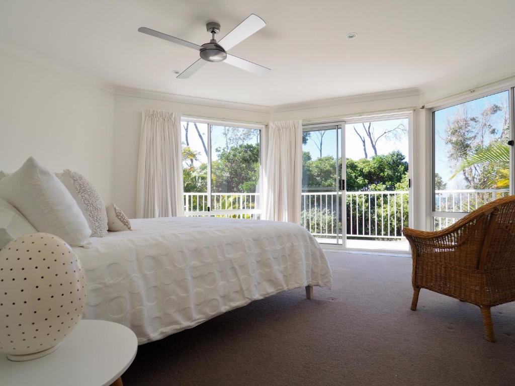 a bedroom with a white bed with a ceiling fan at Beachfront Retreat - Ducted Air - Free Wifi in Coffs Harbour
