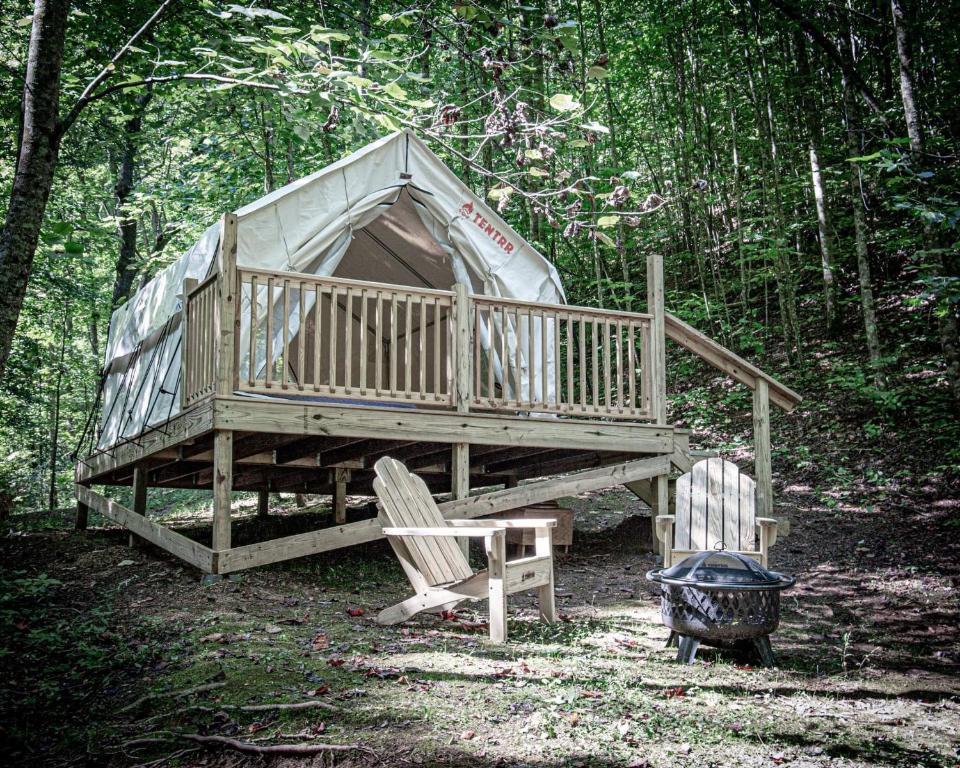 a large wooden house in the woods with two chairs at Tentrr Signature Site - Happy Hollow Hideaway Creekside in Pigeon Forge
