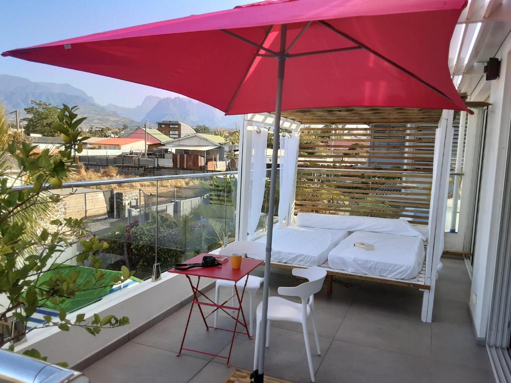 Maison TONGA piscine /jacuzzi chambre de luxe في سانت بيير: مظلة حمراء على شرفة مع سرير وطاولة