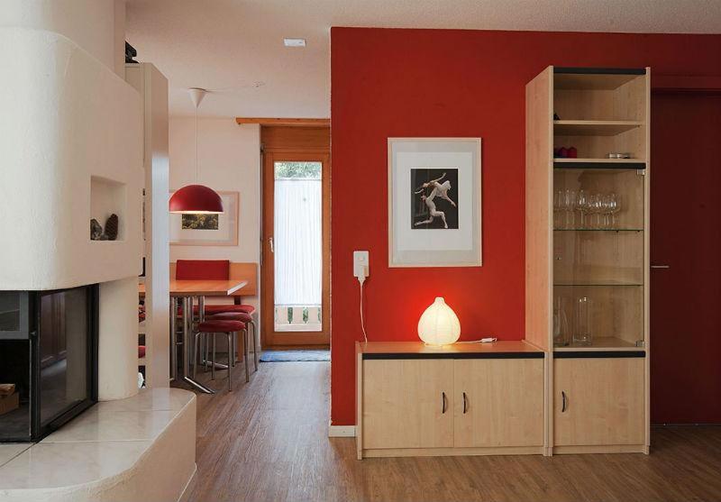 sala de estar con pared roja y cocina en Ferienwohnung Profos 54002B, en Ruschein