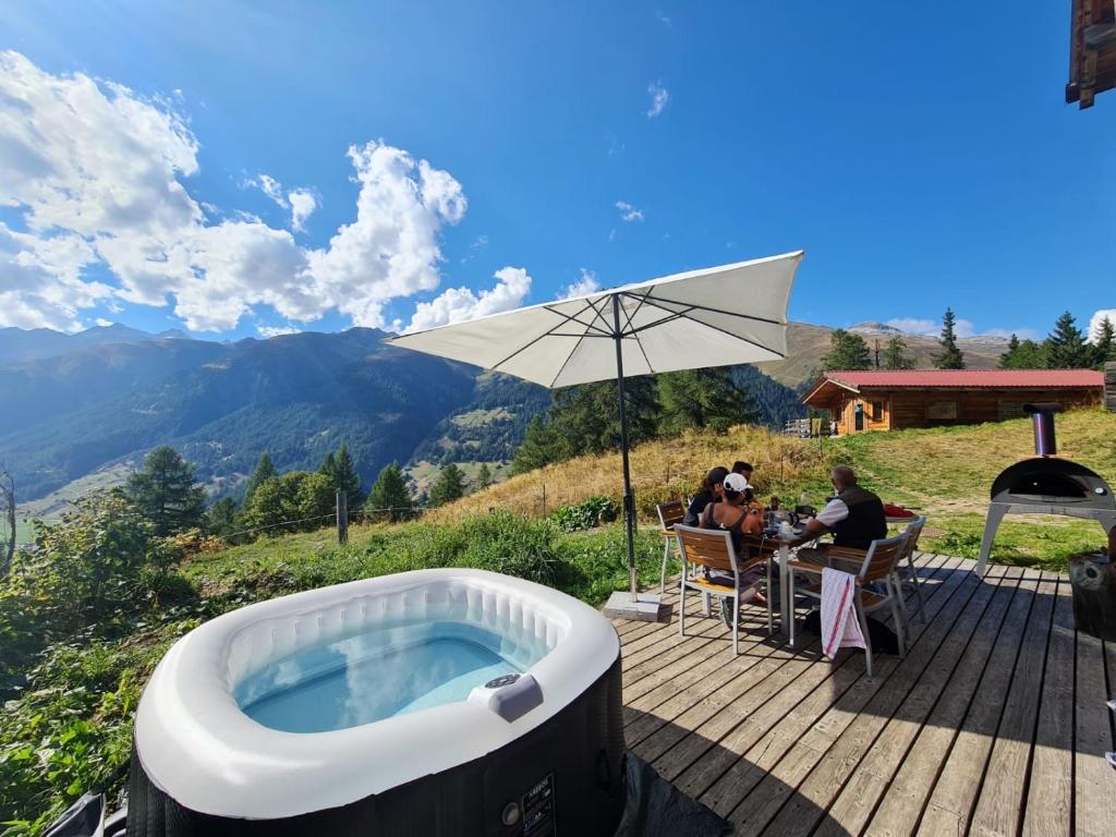 uma banheira de hidromassagem num deque com pessoas sentadas à mesa em Chalet Biene - Swiss Alp Chalet with Sauna and Jacuzzi em Ulrichen