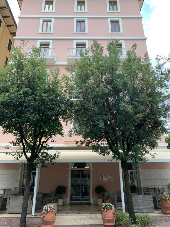 モンテカティーニ・テルメにあるHotel Biondiのピンクの建物の前の二本の木