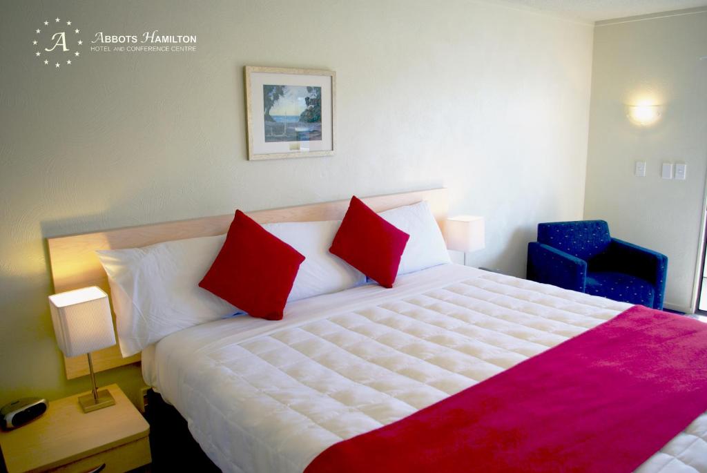 um quarto com uma cama grande e 2 almofadas vermelhas em Abbots Hamilton – Hotel and Conference Centre em Hamilton