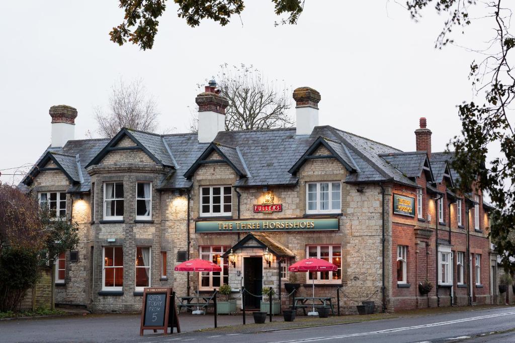 a brick building with red umbrellas in front of it at The Three Horseshoes East Worldham in Alton