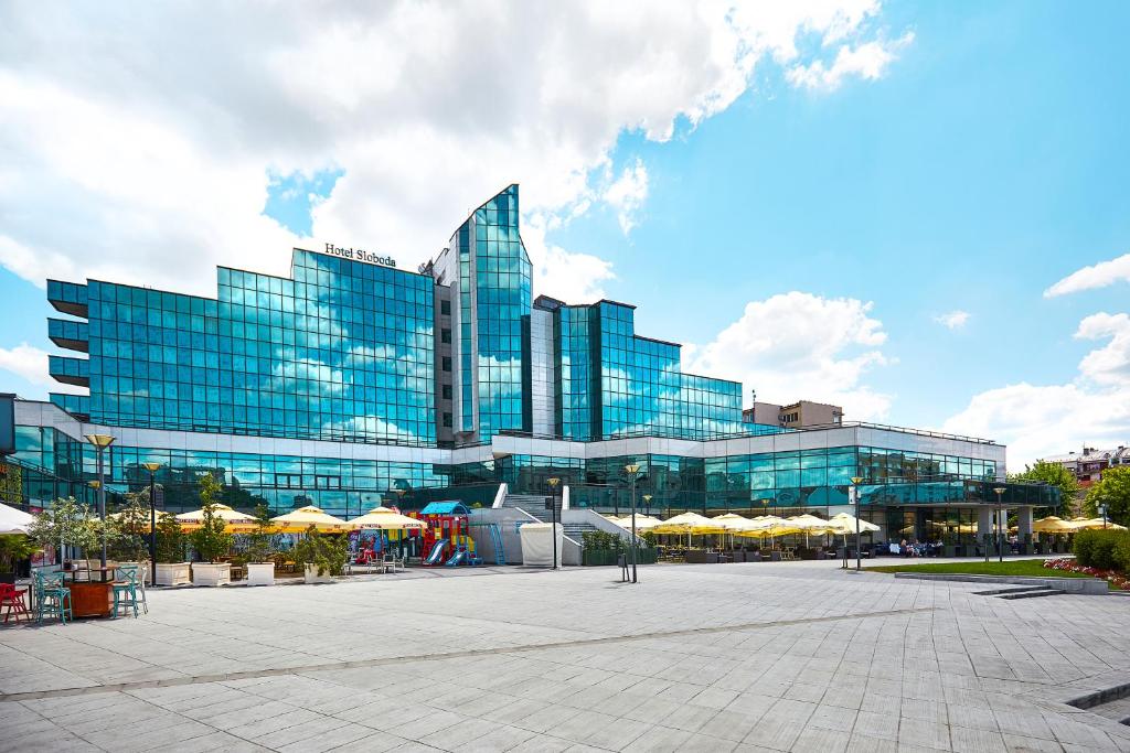 un gran edificio de cristal con sombrillas delante en A Hoteli - Hotel Sloboda en Šabac