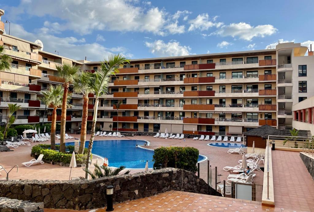 a large apartment building with a swimming pool and palm trees at Gecko apartman in Puerto de Santiago