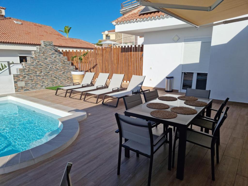 um pátio com uma mesa e cadeiras ao lado de uma piscina em Fantástica Villa Cusmano con piscina privada em Adeje