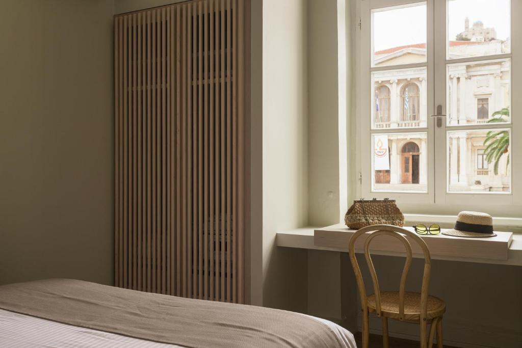 a bedroom with a bed and a window and a chair at SYROS SOUL LUXURY SUITES in Ermoupoli