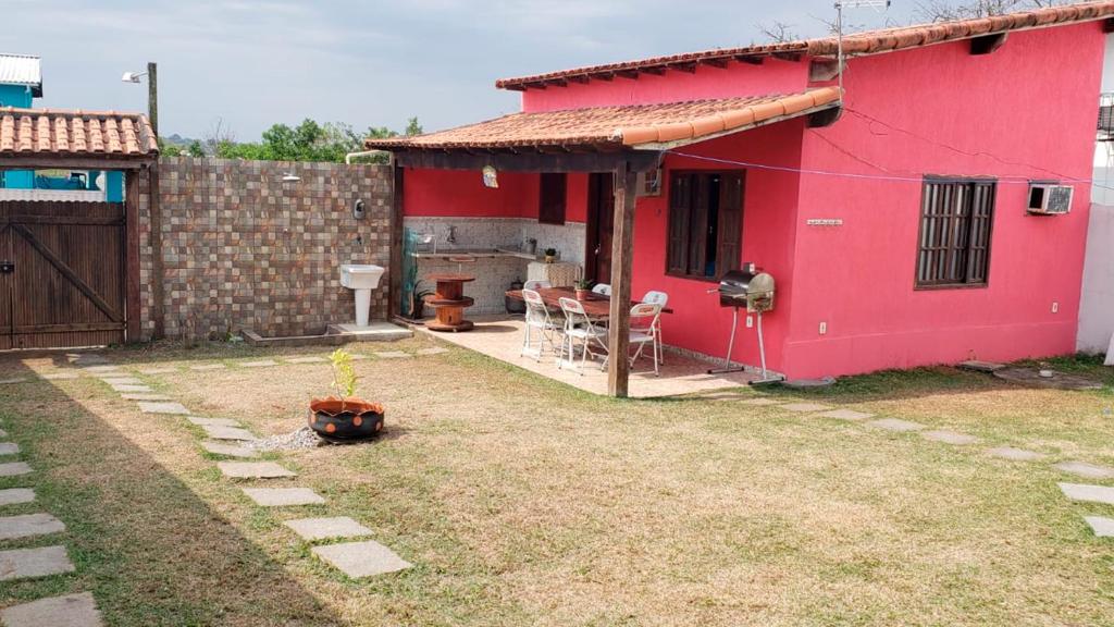 Casa da Dinda à 650m da praia de Itaúna في ساكاريما: منزل احمر مع طاولة وكراسي في ساحة