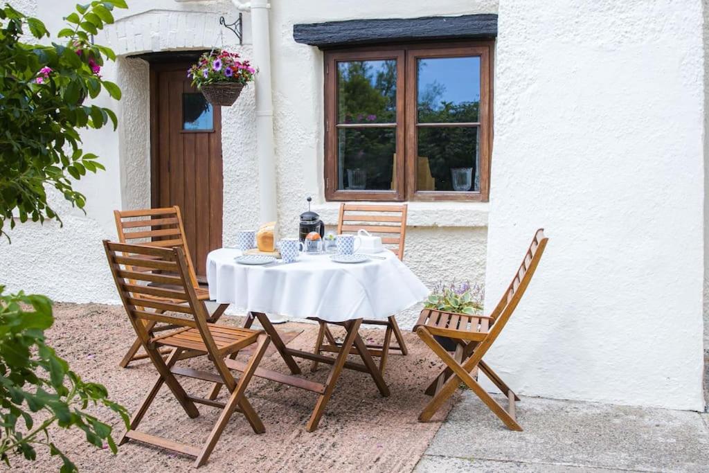 una mesa con un mantel blanco y sillas frente a una casa en Batney Farm Cottage, Meshaw, South Molton, en South Molton