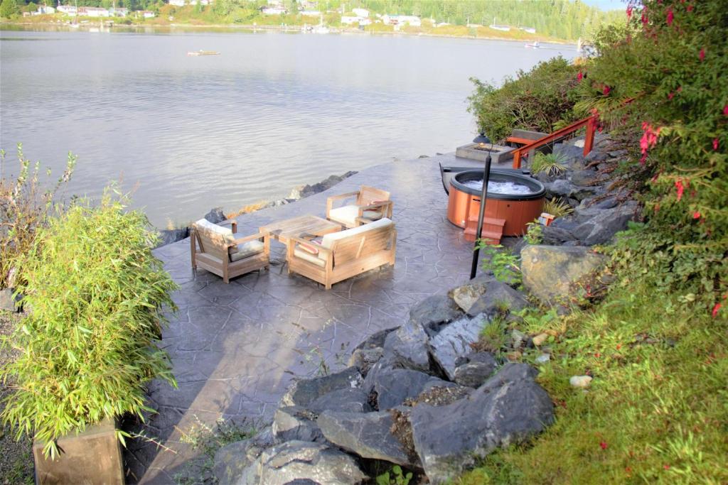 dos sofás y una hoguera junto a un cuerpo de agua. en Salt Loft - Oceanfront, Hot Tub And Firepit!, en Ucluelet