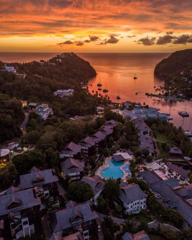 Sunset aerial view of coastal resort with pool, buildings, and anchored sailboats.