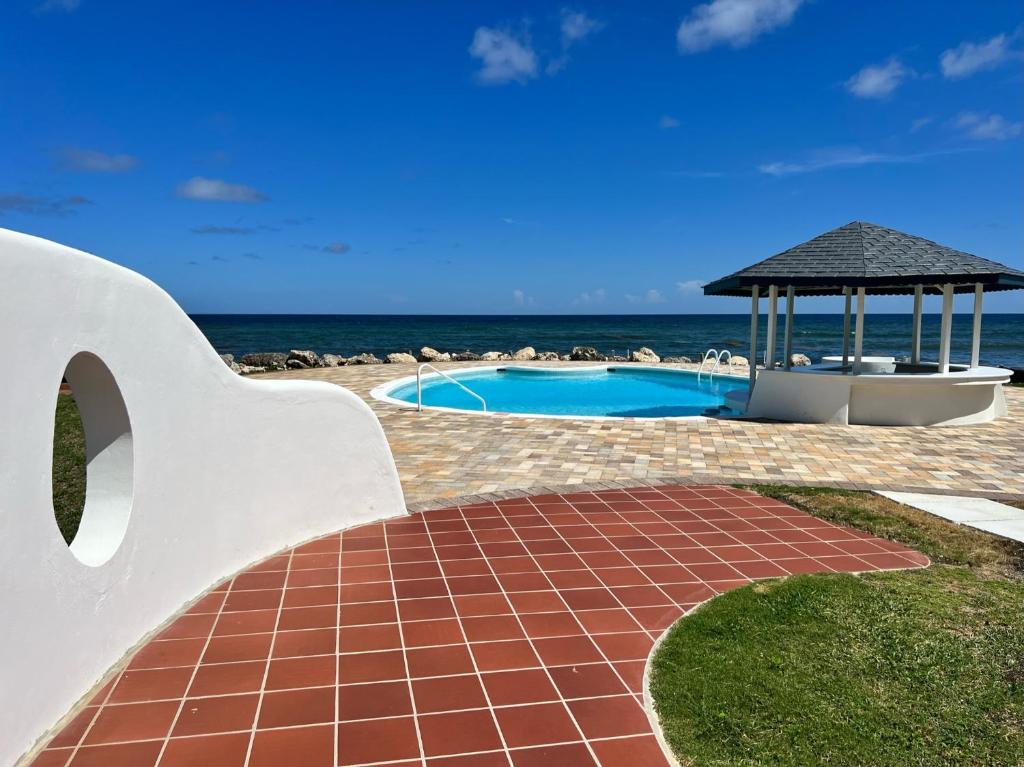 a swimming pool with a gazebo next to the ocean at OceanBlue Resort in Christ Church