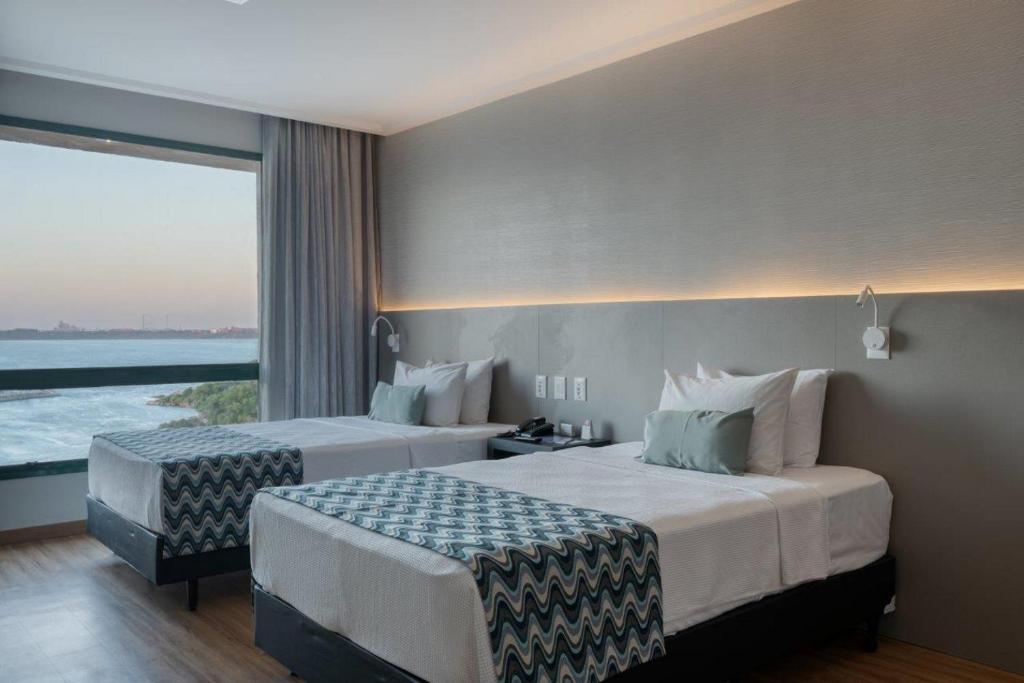 a hotel room with two beds and a large window at Comfort Suítes Vitória in Vitória