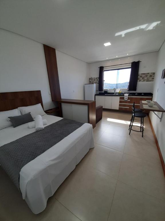 a bedroom with a bed and a desk and a window at Alpes Flats in Campos do Jordão