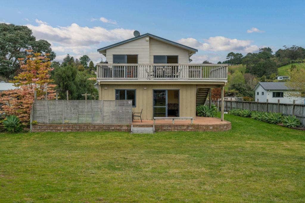 a house with a balcony on top of a yard at Hosts on the Coast Laze Away on Cook in Cooks Beach