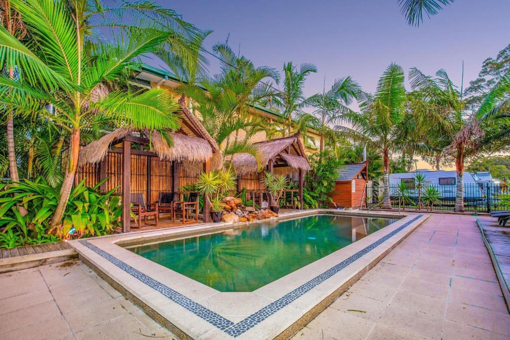 a swimming pool in front of a house with palm trees at River Retreat Home & Holiday Park in Tweed Heads