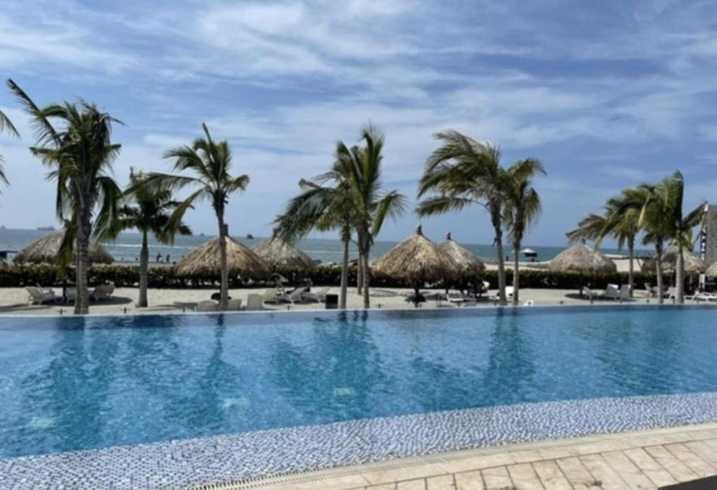 una piscina con palmeras y sombrillas de paja en Samaria - Apartamento en Club de Playa, Santa Marta, en Santa Marta