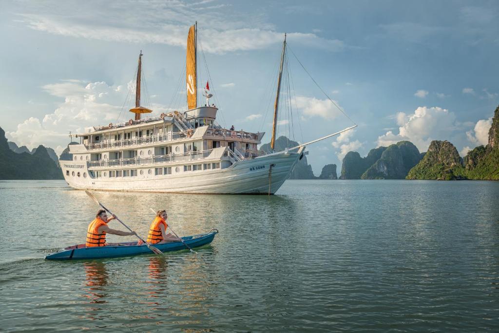 two men in a kayak in front of a cruise ship at Paradise Sails Cruise in Ha Long