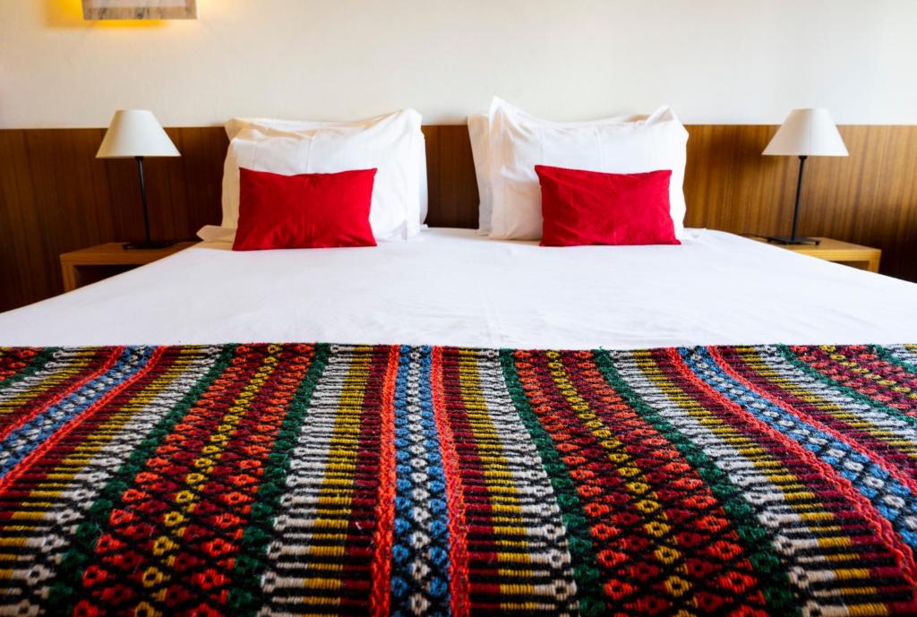 a bed with two red pillows and a colorful blanket at Hotel Apartamento Porto Covo in Porto Covo
