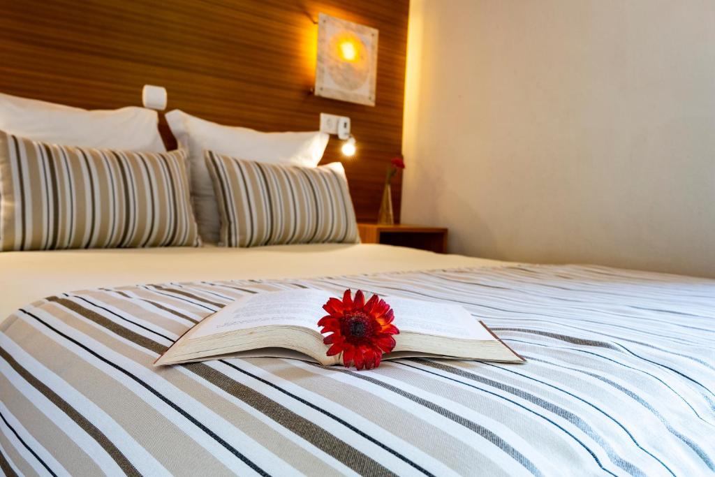 a book with a red flower sitting on top of a bed at Hotel Apartamento Porto Covo in Porto Covo