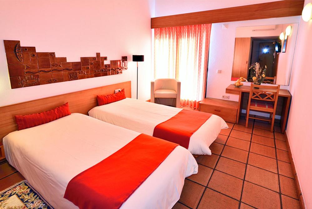 a hotel room with two beds and a desk at Hotel Apartamento Porto Covo in Porto Covo