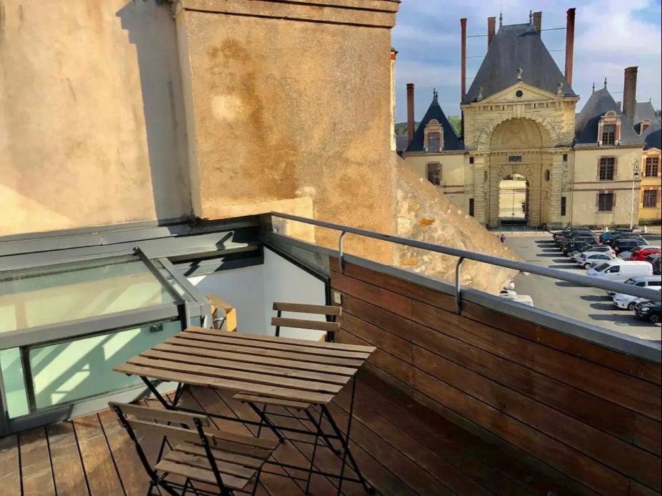 un banc en bois assis sur un balcon d'un bâtiment dans l'établissement Suites Rive Gauche - Vue Château Fontainebleau - Chez Lydia, à Fontainebleau