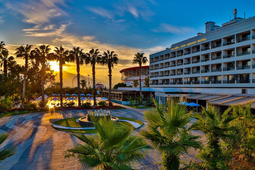 Nashira City Resort Hotel في أنطاليا: فندق فيه نخل قدام غروب الشمس