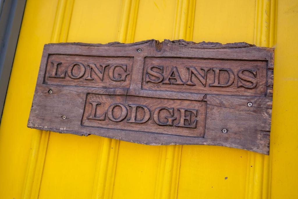 un cartello che legge "Lunghe Sabbie Lodge" su un muro giallo di Longsands Lodge a Tynemouth