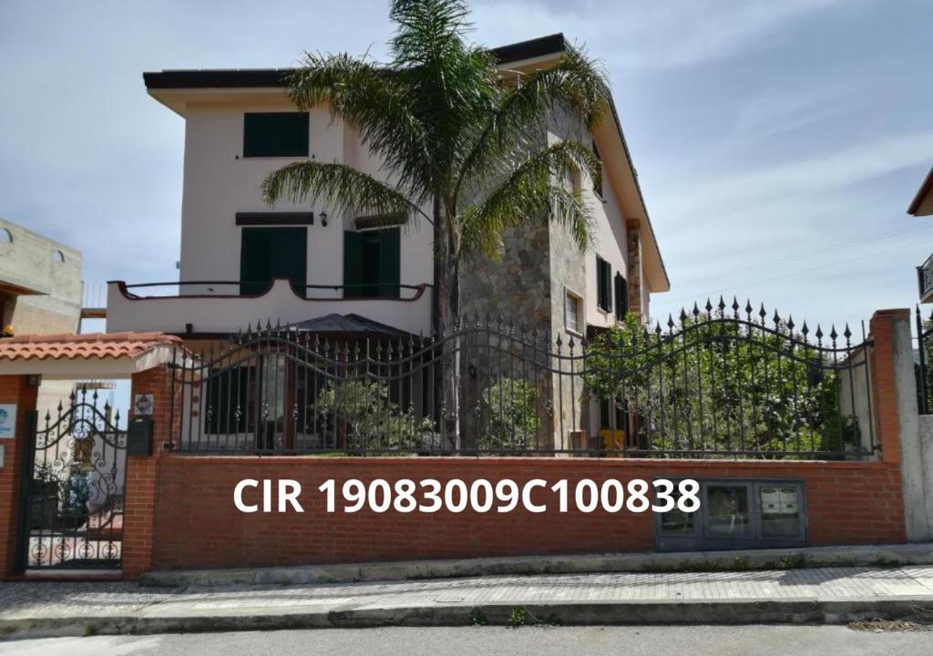 a building with a palm tree in front of a fence at La Collina Capo d'Orlando in Capo dʼOrlando