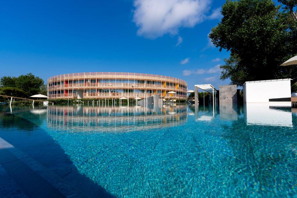 un edificio con una piscina d'acqua di fronte ad esso di Isola di Albarella Hotel Capo Nord a Isola Albarella