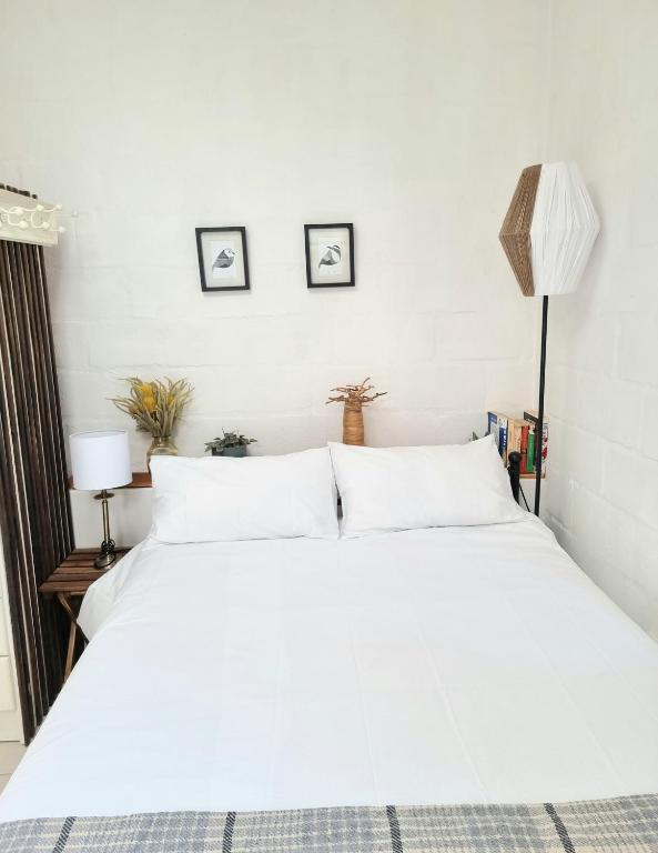 a white bed in a bedroom with three pictures on the wall at Sunlight Cottage in Cape Town