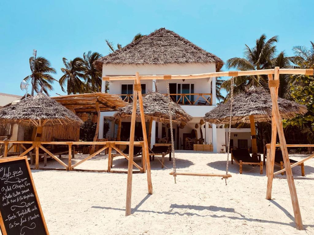 een resort met rieten parasols en een bord op het strand bij Helwas Zanzibar Beach Hotel in Bwejuu