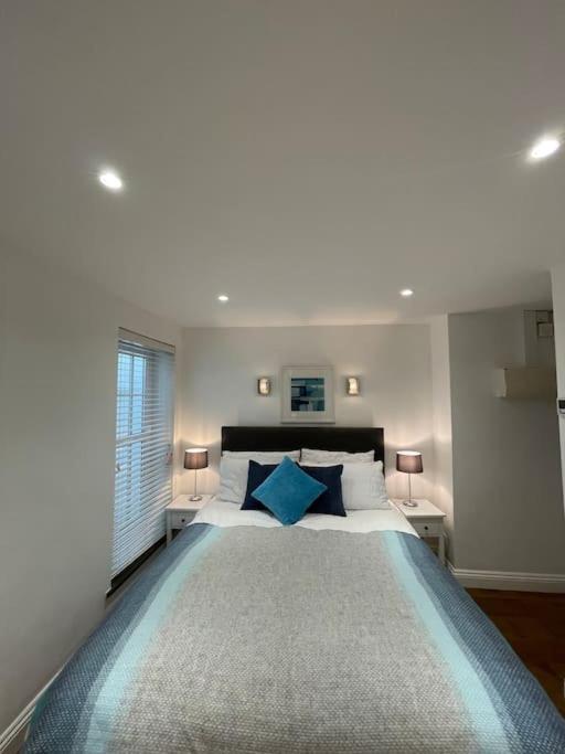 a white bedroom with a large bed with blue pillows at Fuchsia Cottage in Flushing