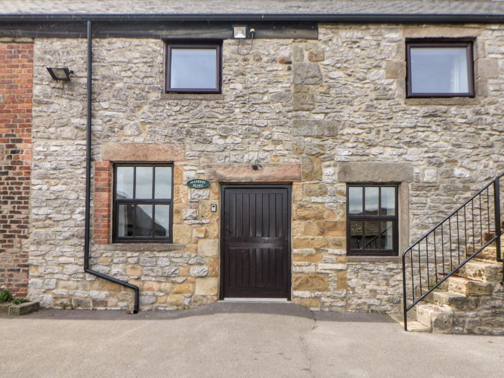 a stone building with a black door and windows at Haddon Cottage in Bakewell